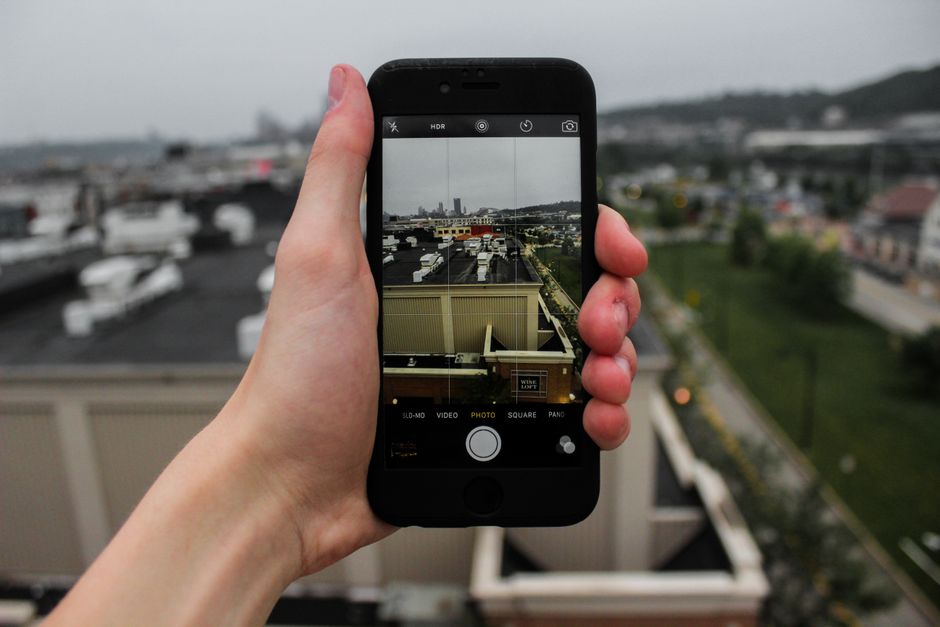 A hand holding a smartphone capturing an urban cityscape from a rooftop view.